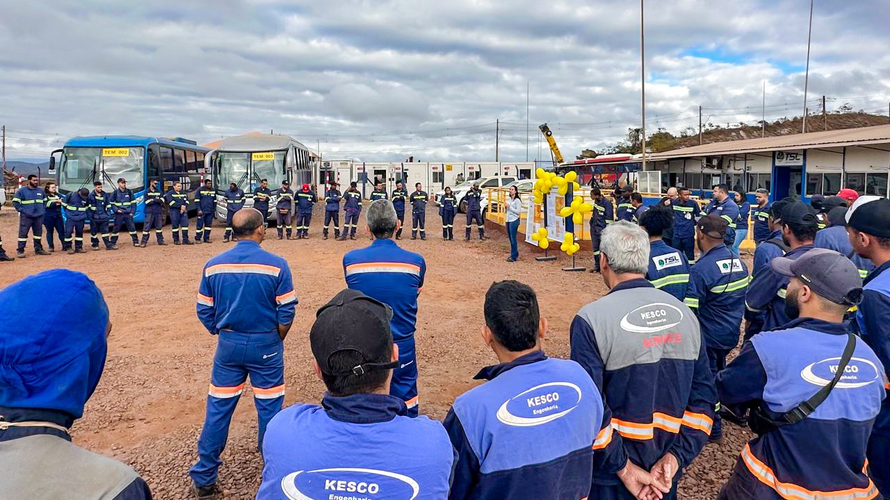 Equipes reunidas em roda para um Diálogo de Segurança, em frente ao painel da campanha