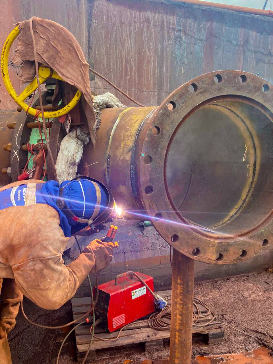 Soldador executando solda na junta de um flange de tubulação de grande diâmetro